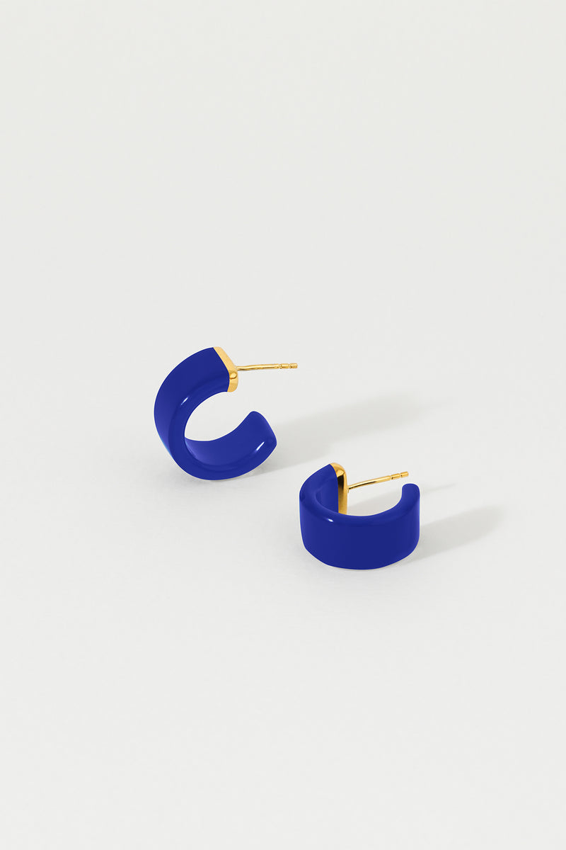 A pair of indigo huggie earrings with 18K gold plated sterling silver studs on a white background.