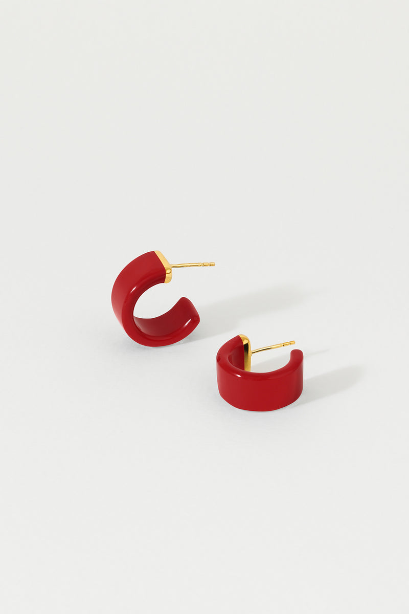 A pair of tomato red huggie earrings with 18K gold plated sterling silver studs on a white background.